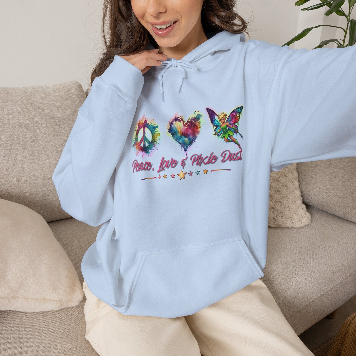A woman wearing a light blue hoodie with a colorful peace-themed graphic on the chest, sitting on a beige couch.